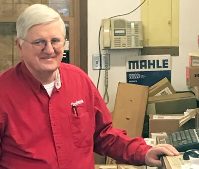 Man with white hair and wearing red button down shirt standing at a counter