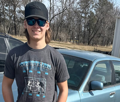 teen boy wearing black ball cap and sunglasses posing in front of 1993 Grand Marquis car