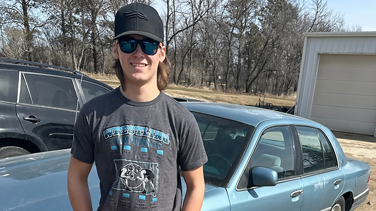 teen boy wearing black ball cap and sunglasses posing in front of 1993 Grand Marquis car