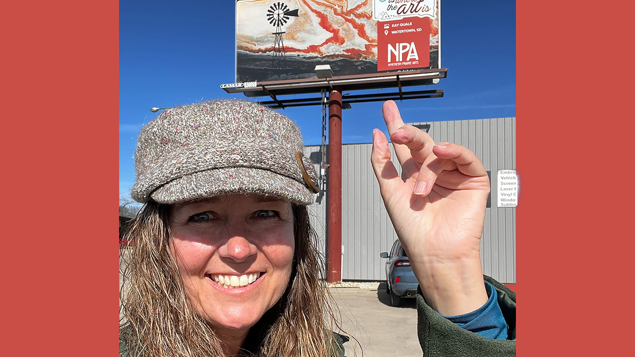 Kay Quale pointing to a billboard behind her