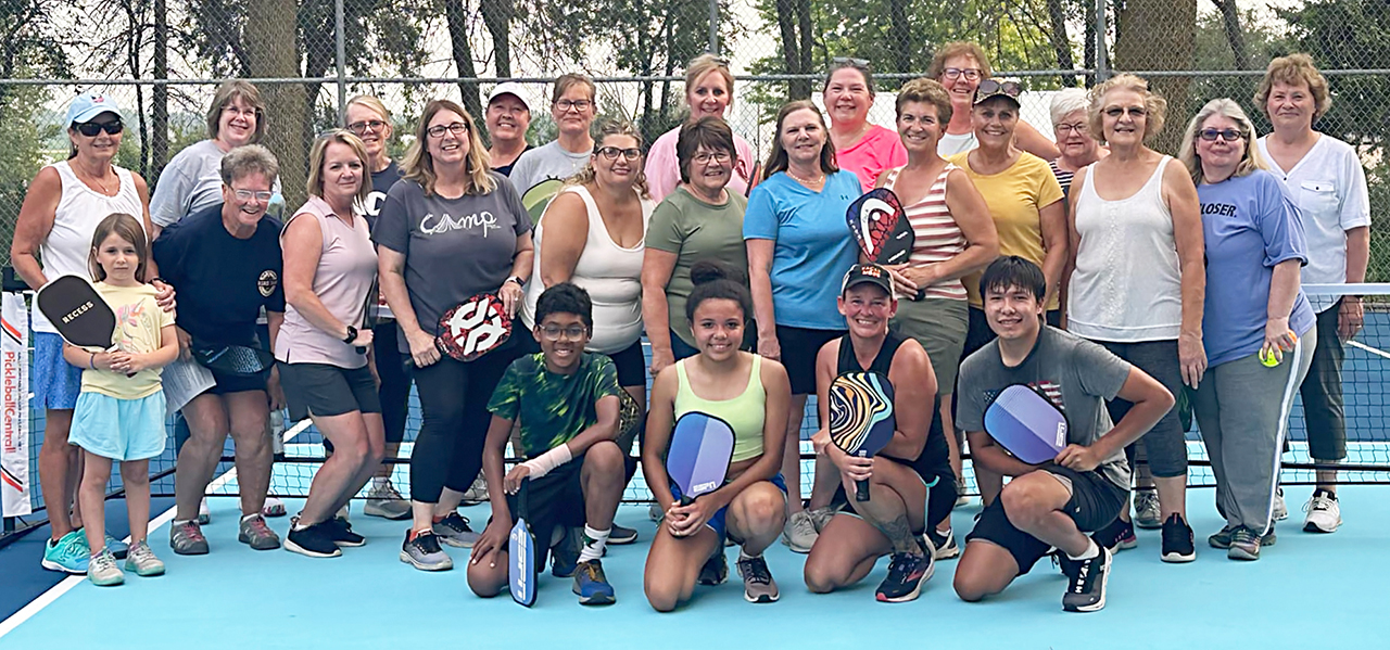 several people posed together on a pickleball court