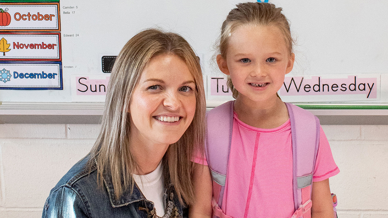 adult woman in denim jacket with young girl wearing purple backpack and pink tee shirt