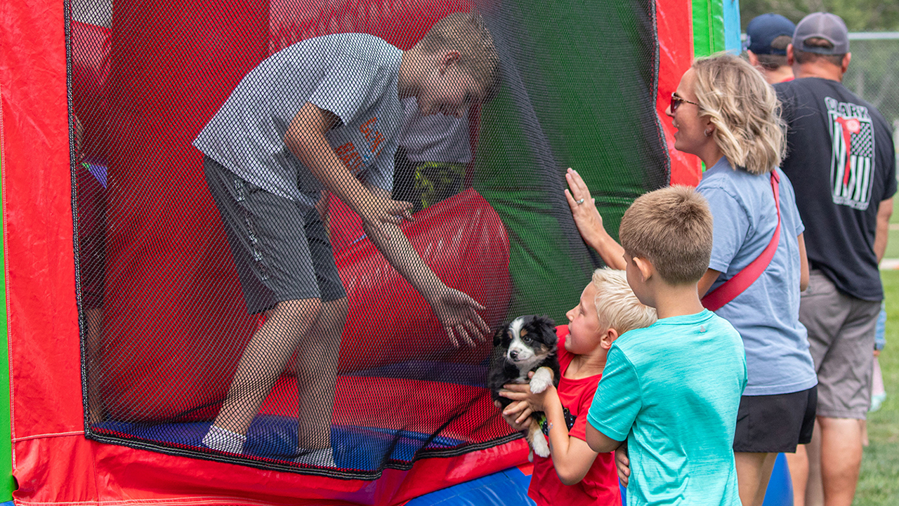 child in bounce house looking at brown and white puppy held by another child outside the toy