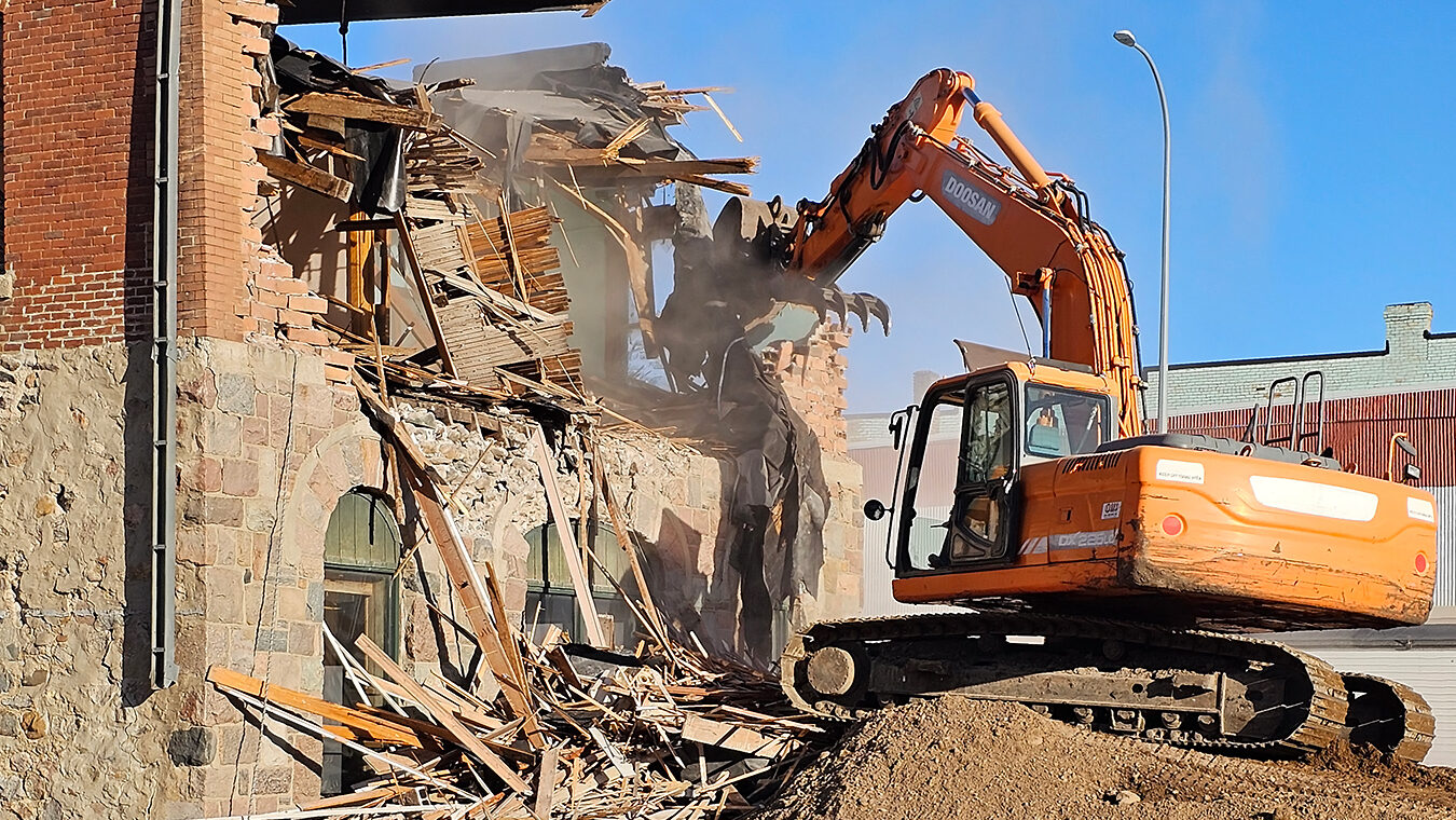 operating crane tearing down historic brick building