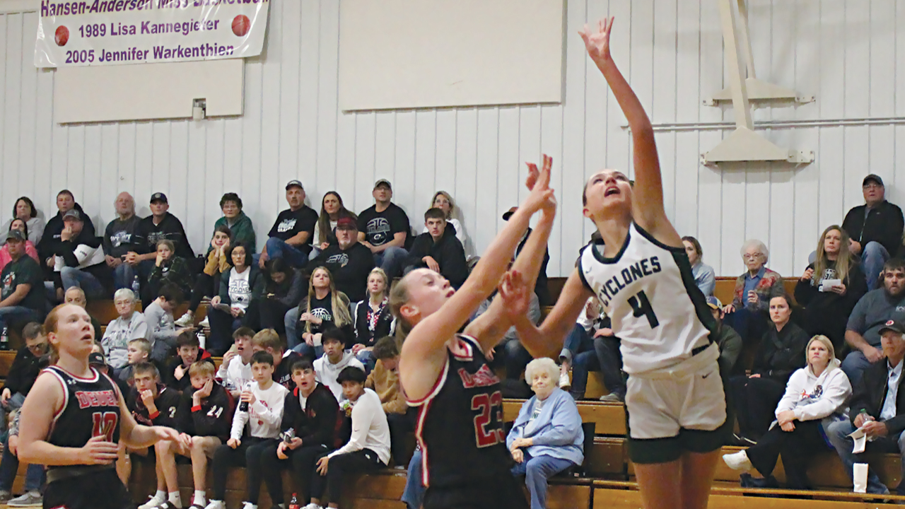 three female basketball players with two in black uniforms and one in white that is jumping