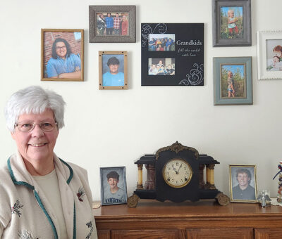 mildred saboe standing in front of grandchildren's photos