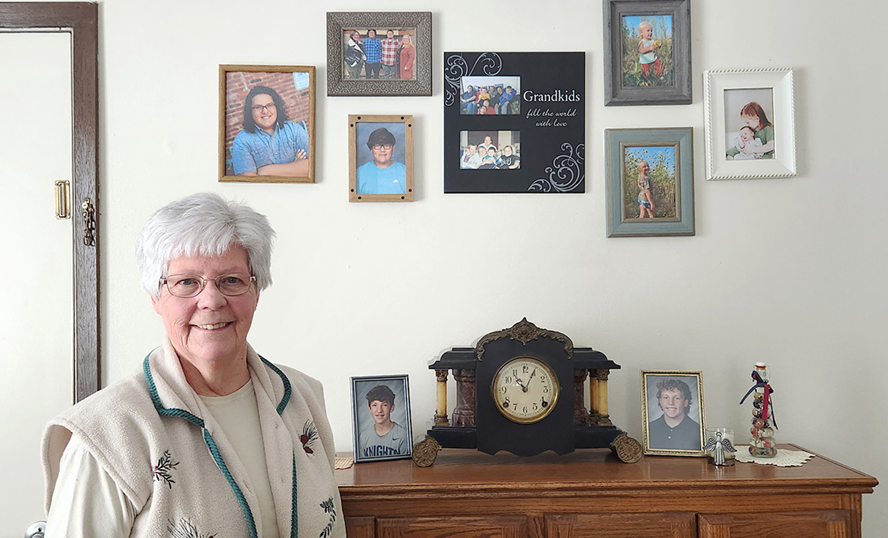 mildred saboe standing in front of grandchildren's photos