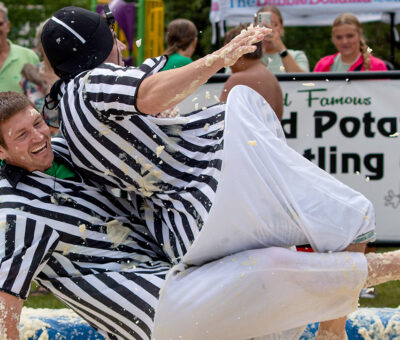 two men in striped referee shirts wrestling in mashed potatoes